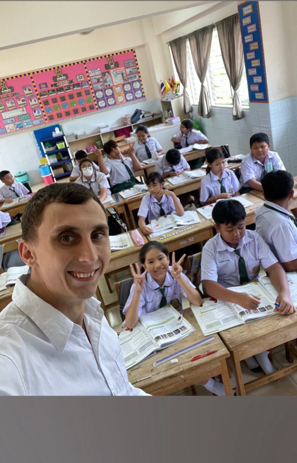 Roman taking a selfie at the front of a Thai classroom full of uniformed students at their desks.